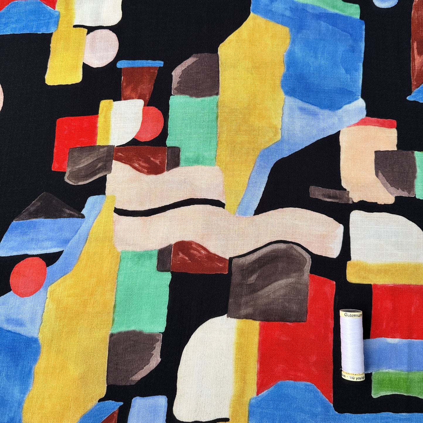 Reel of thread for scale on a fabric with a colourful abstract pattern on a black background