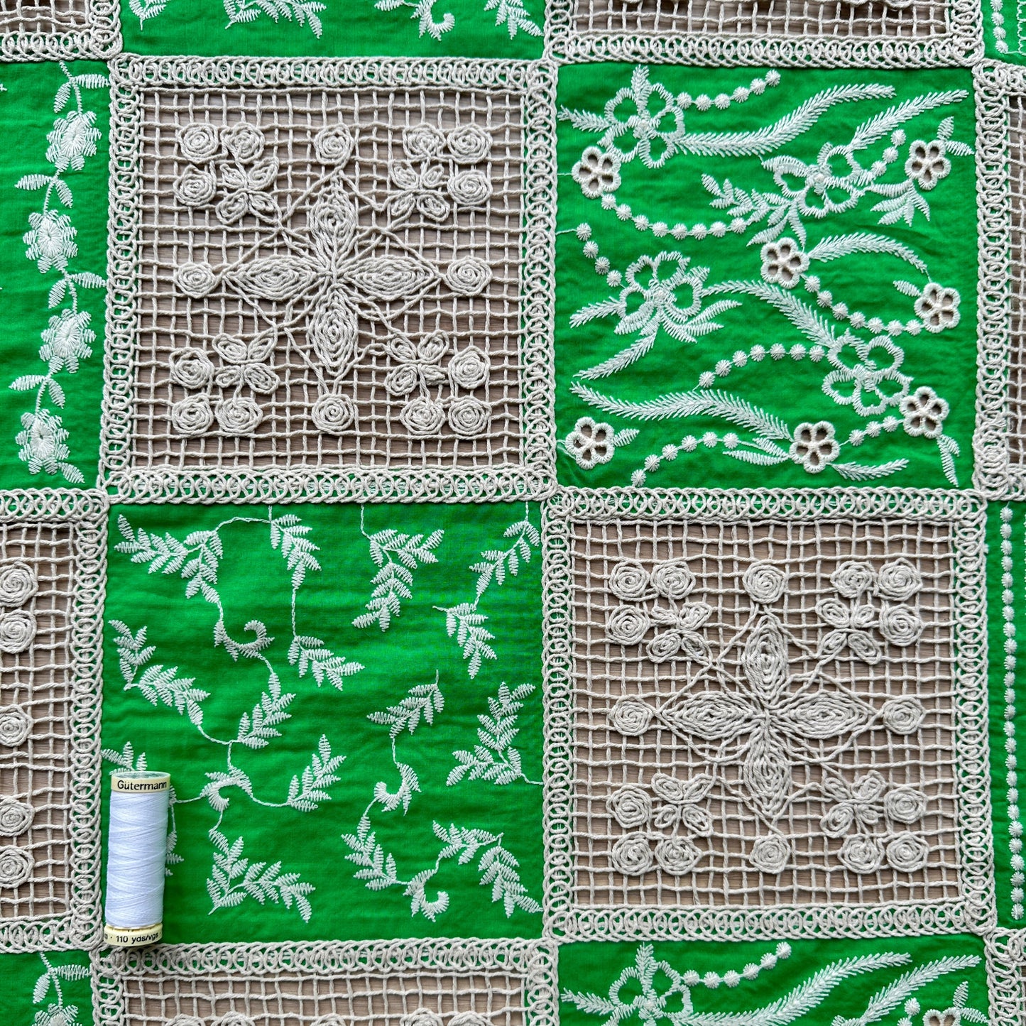 Green and beige fabric with floral lace patterns with a reel of thread for scale