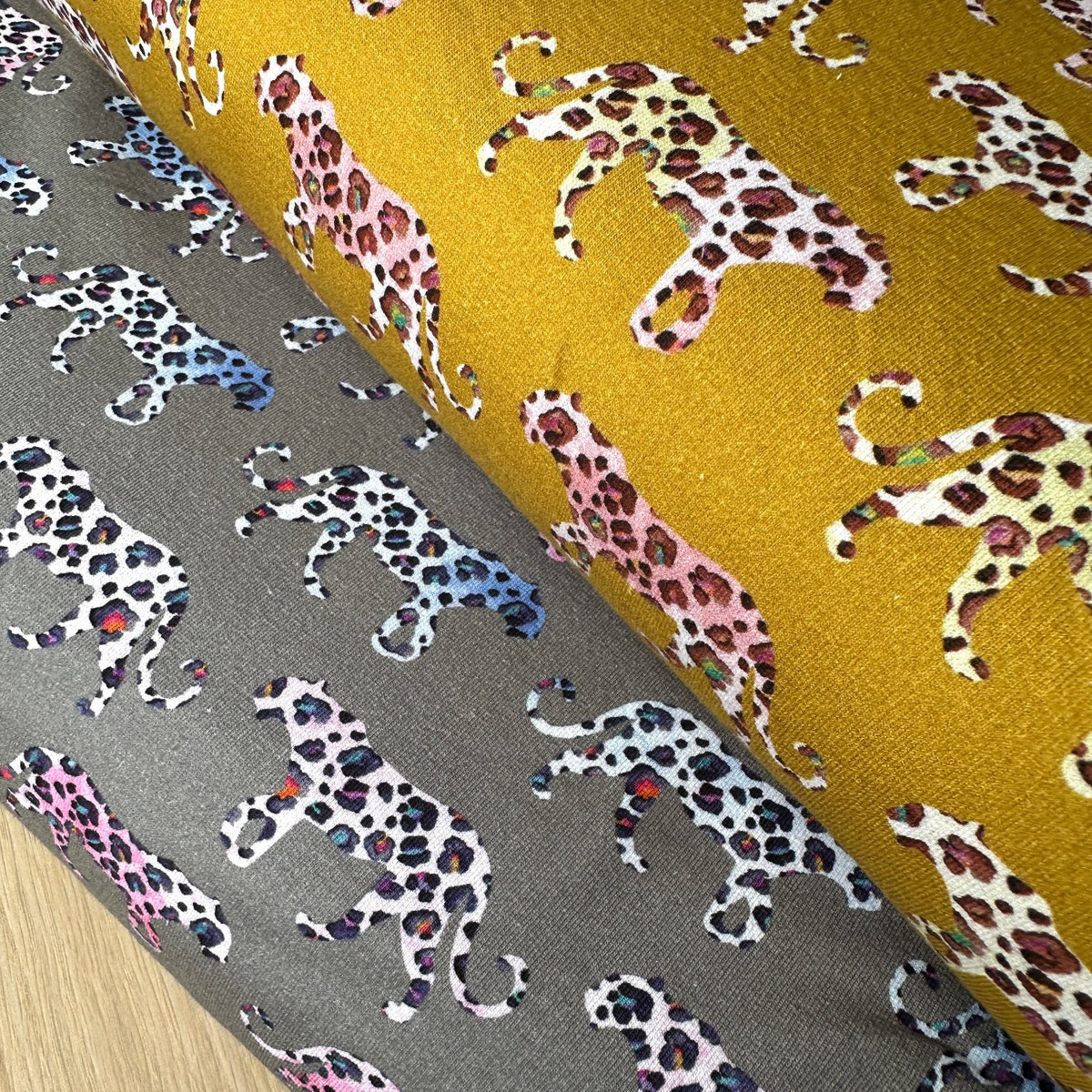 Two bolts of french terry fabric in grey and mustard with colourful leopards walking across them