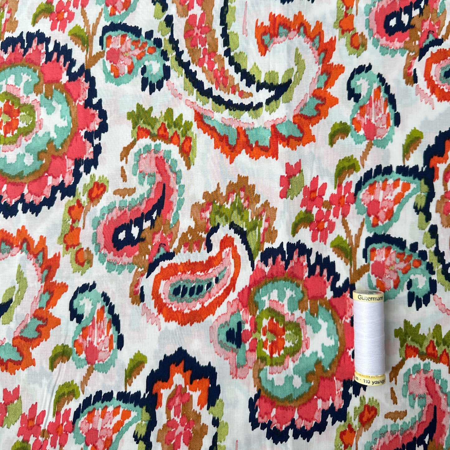 Watercolour Paisley Pima Cotton Lawn Fabric in Coral with reel of thread for scale
