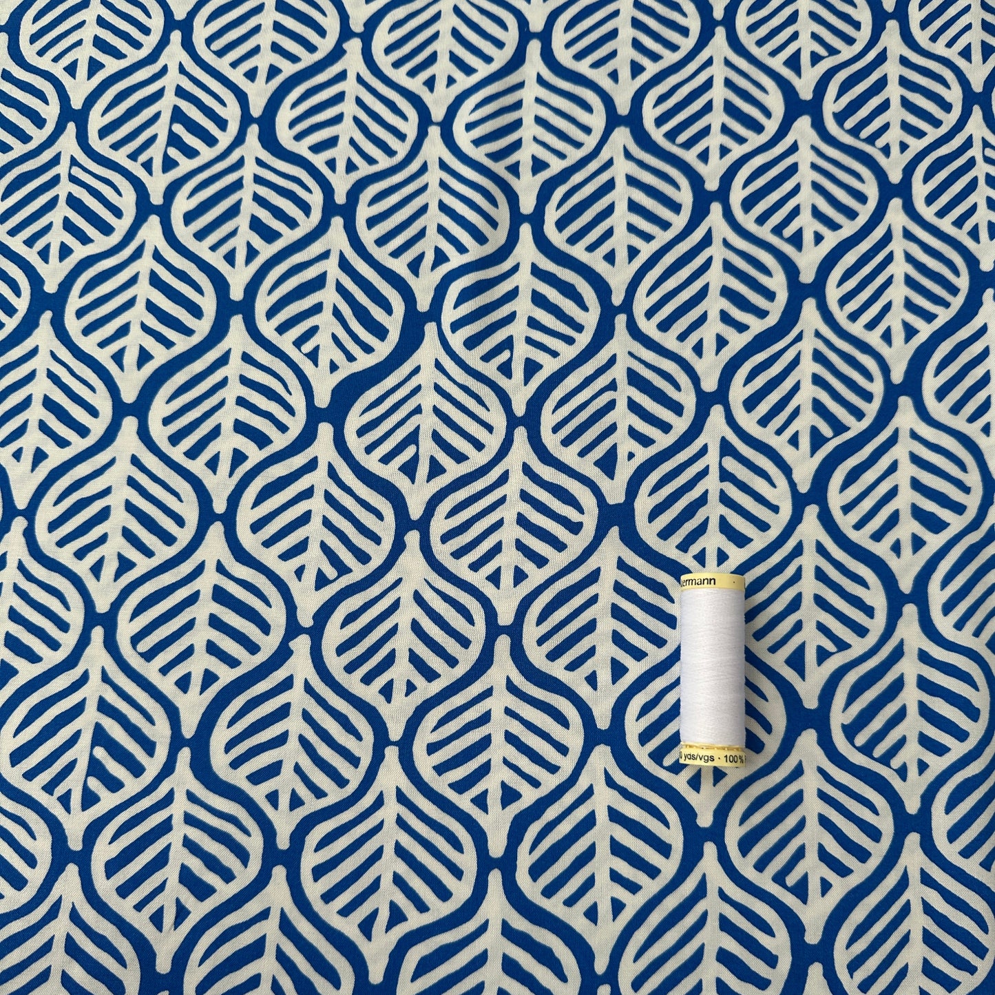 White leaves on cobalt blue viscose fabric with reel of thread for scale