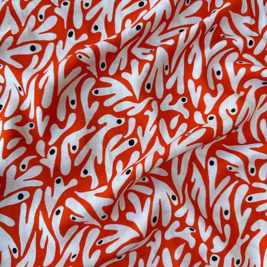 Dressmaking fabric with an abstract pattern in off white and black on an orange background