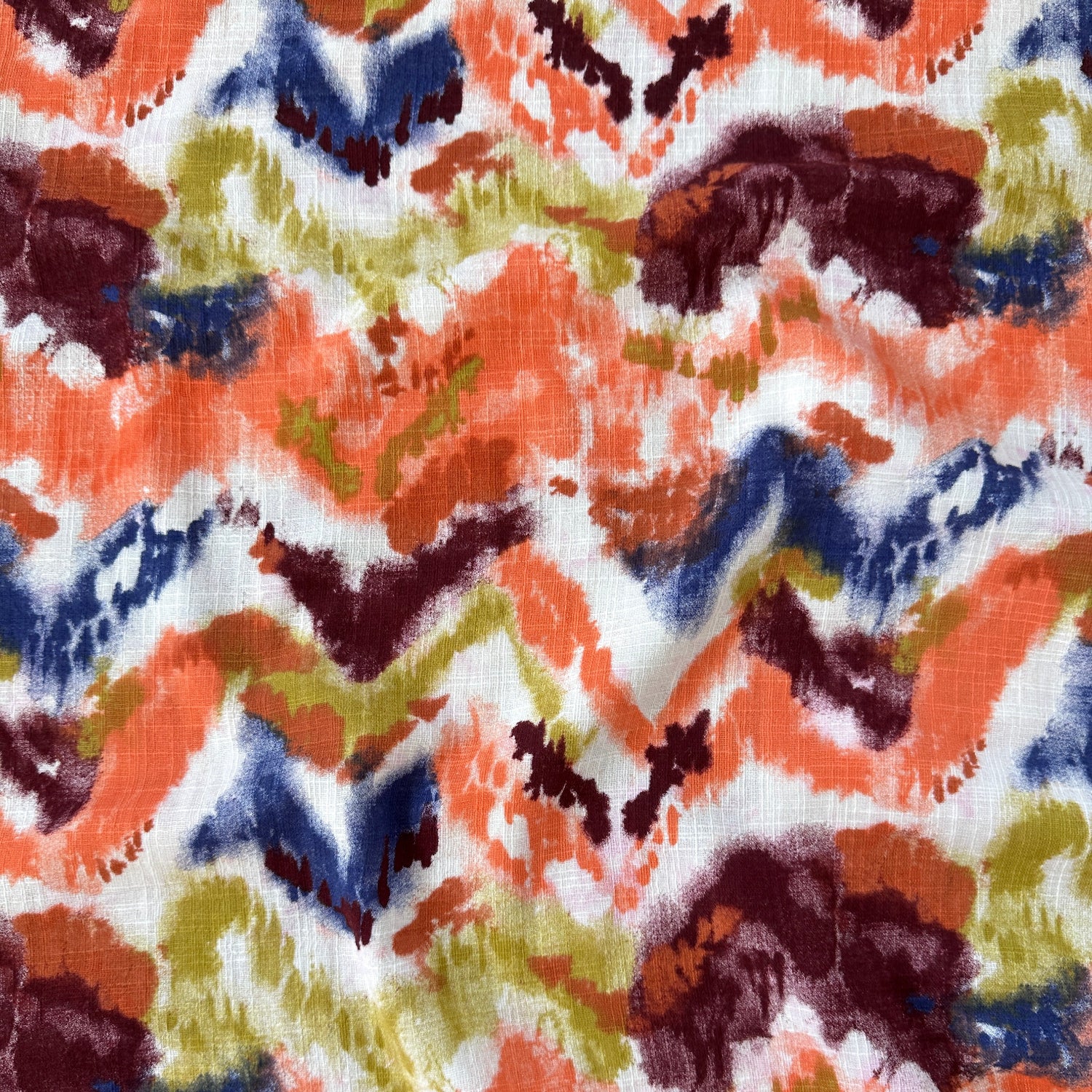 A close-up of a fabric with an abstract, multicolour chevron pattern featuring orange, navy blue, olive green, burgundy and white.
