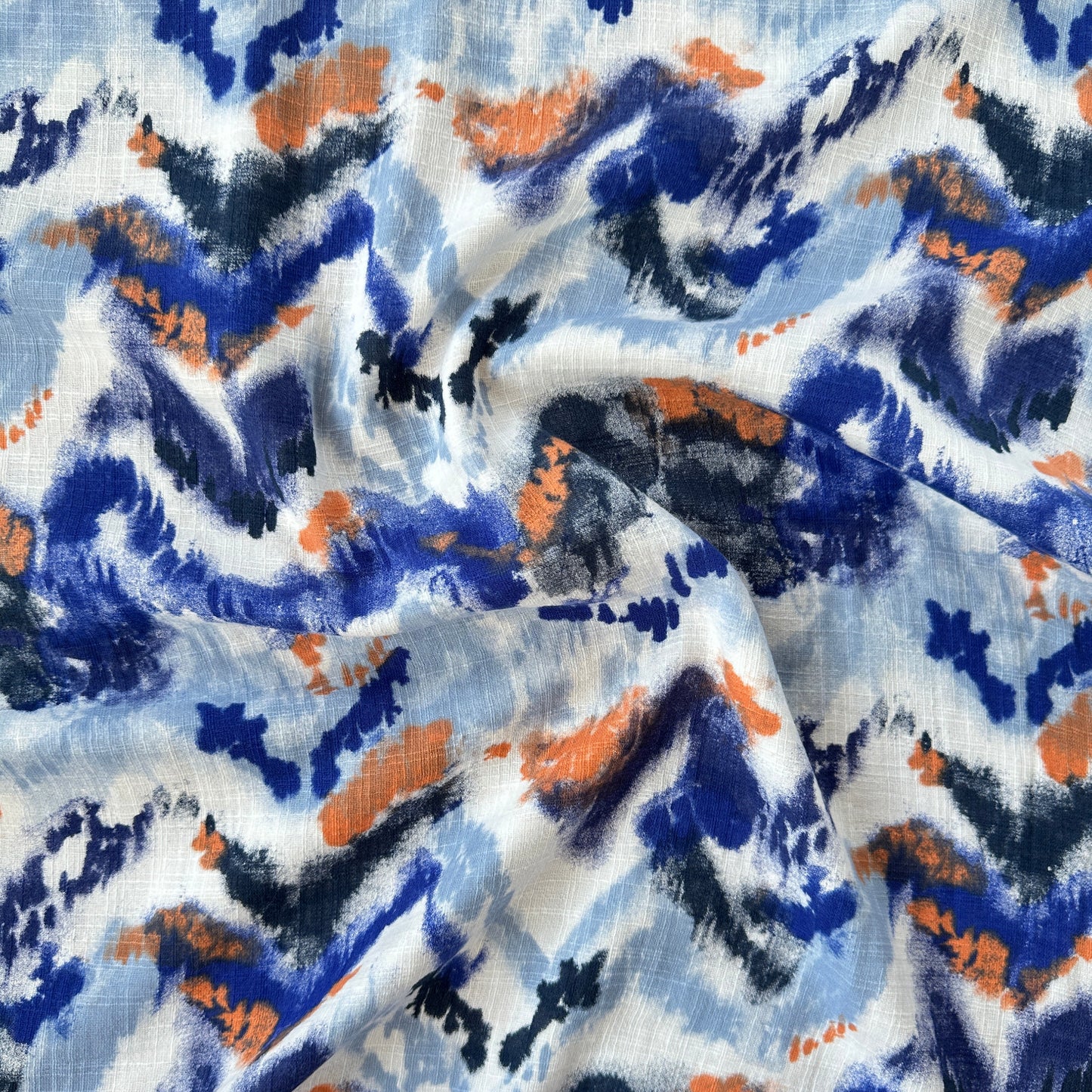 A close-up of draped fabric with an abstract watercolour-style print in blue, navy, orange, black, and white.