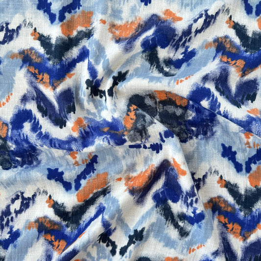 A close-up of draped fabric with an abstract watercolour-style print in blue, navy, orange, black, and white.