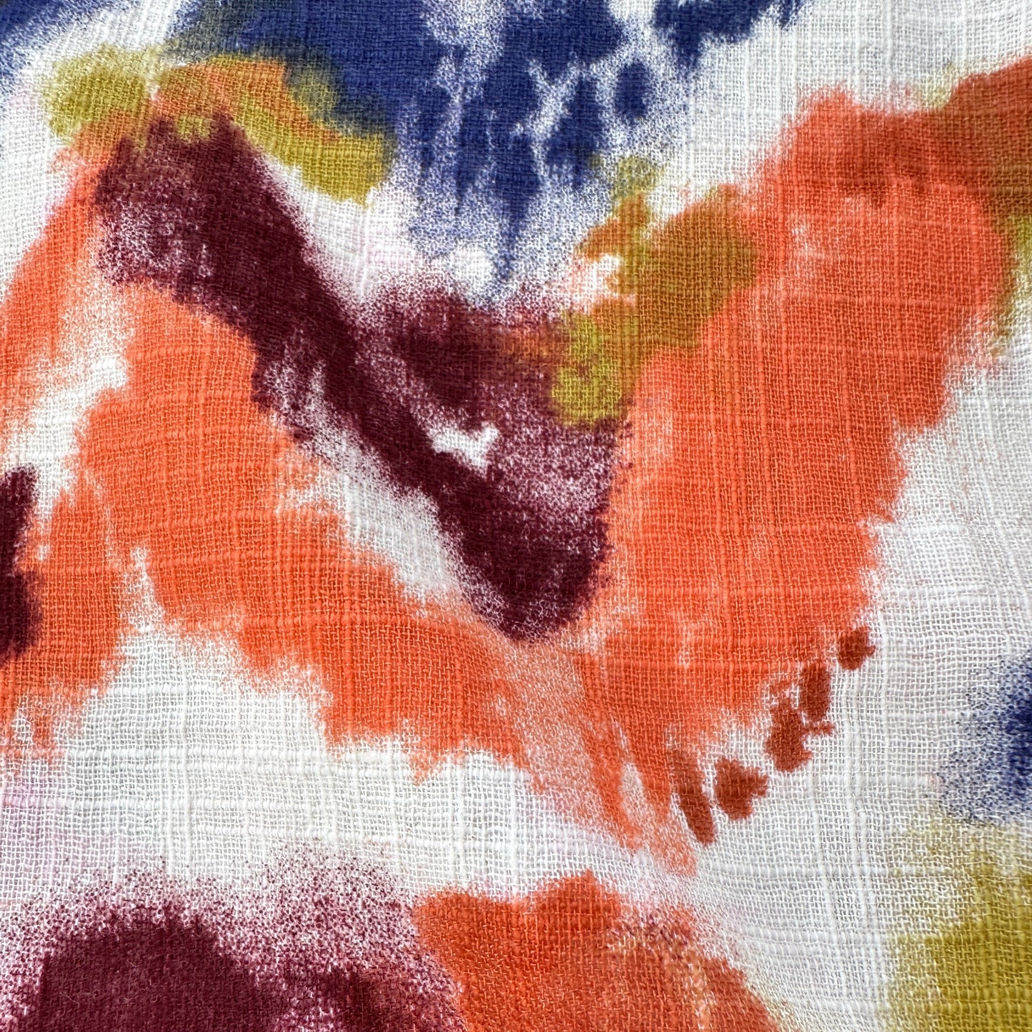 A close-up of a textured fabric with an abstract watercolor pattern in orange, dark burgundy, navy blue, olive green, and white.
