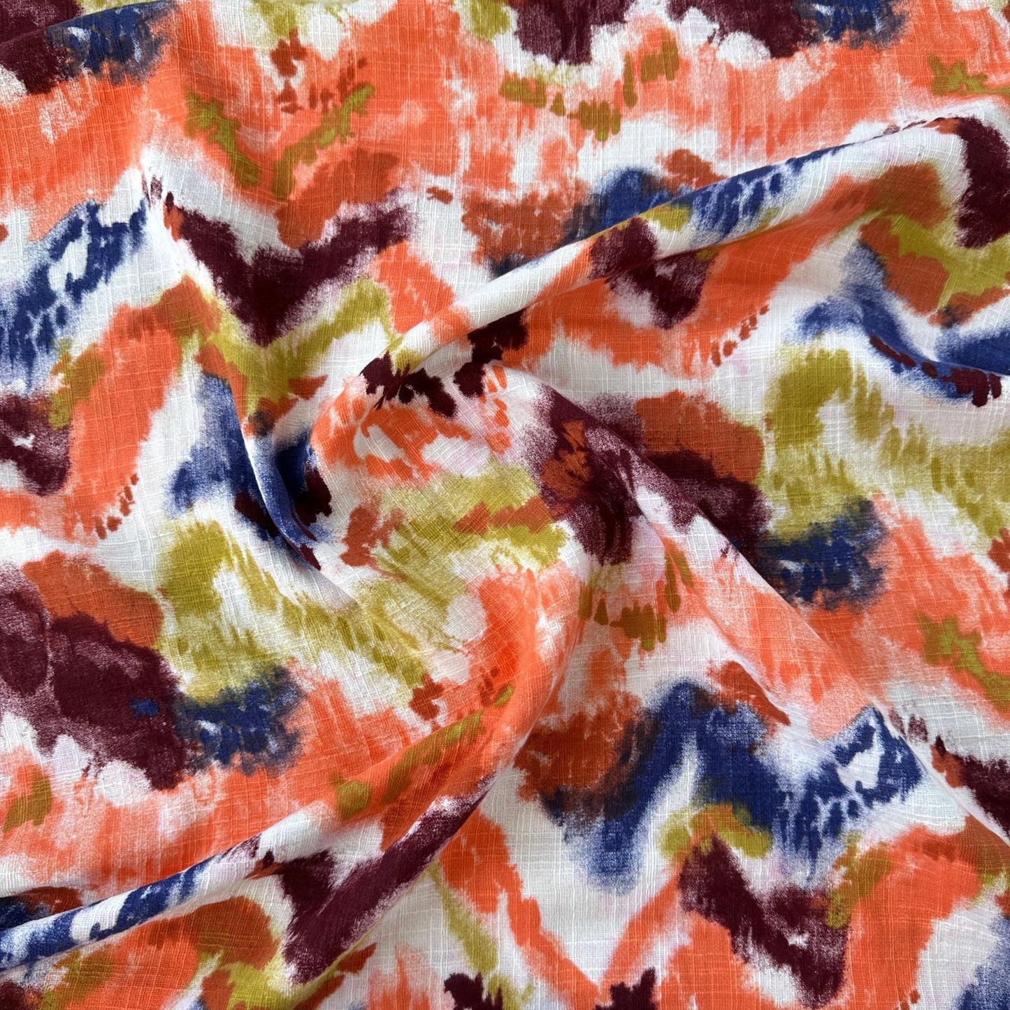 A close-up of draped fabric with an abstract zigzag pattern in orange, navy blue, olive green, burgundy, and white.