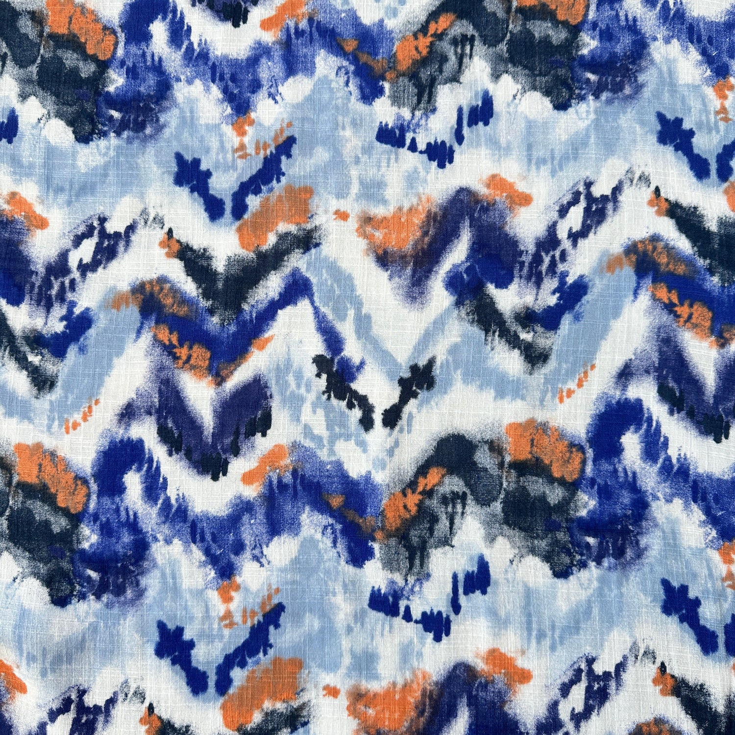 A close-up of a fabric pattern featuring an abstract, watercolor-like design with zigzag and brushstroke elements in blue, navy, orange, and white.