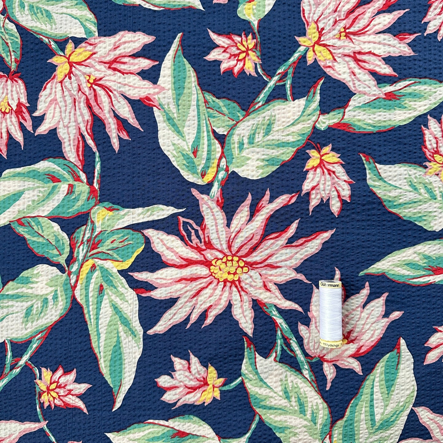 Reel of thread showing scale of Floral pattern with pink flowers and green leaves on a blue background