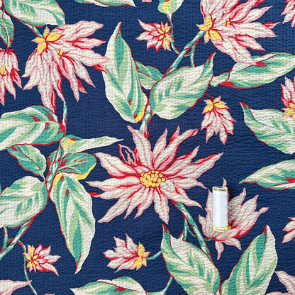 Reel of thread showing scale of Floral pattern with pink flowers and green leaves on a blue background