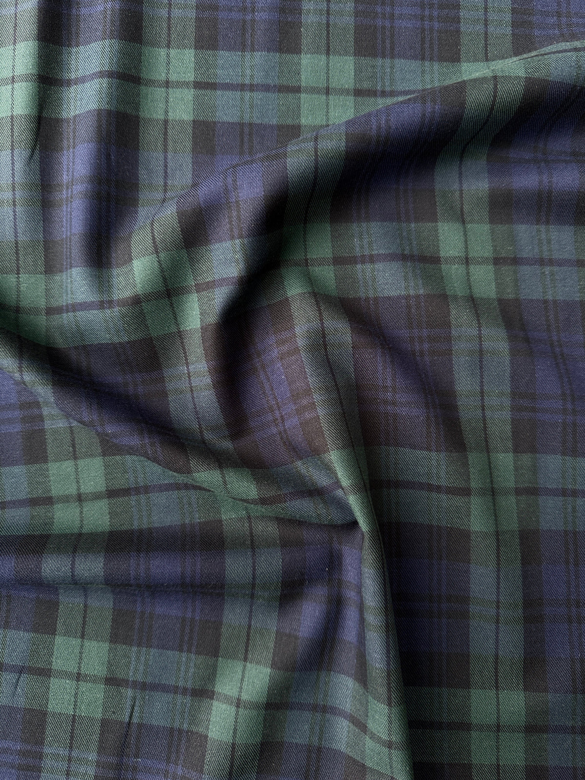 A close-up of draped fabric with a plaid pattern in green, navy and black