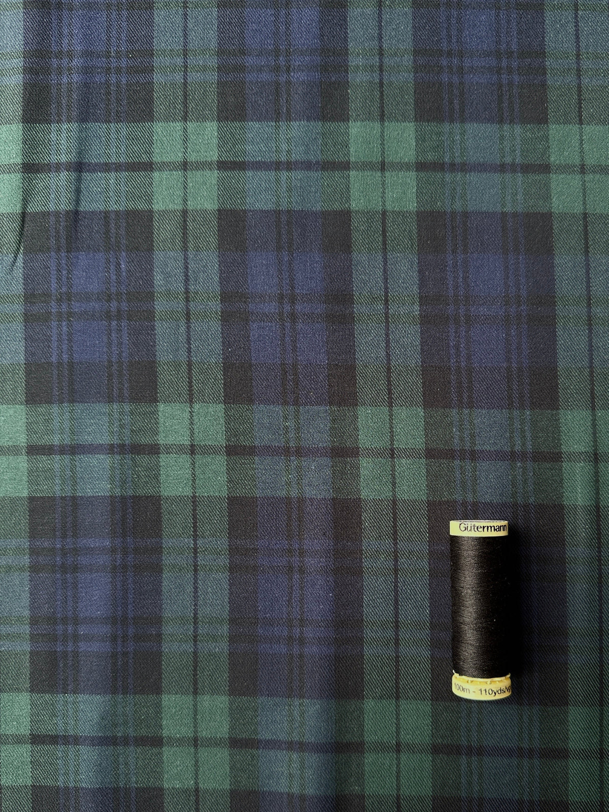 Reel of black thread on black watch cotton twill tartan fabric for scale