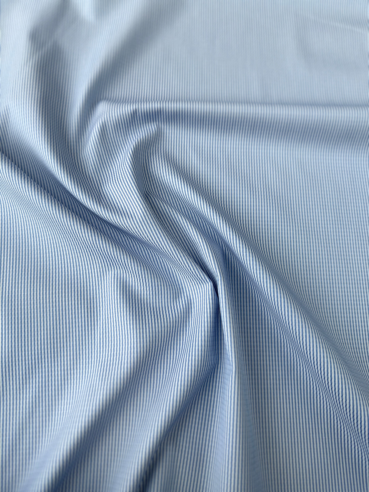 Light blue and white striped fabric draped in soft folds to show texture and pattern.