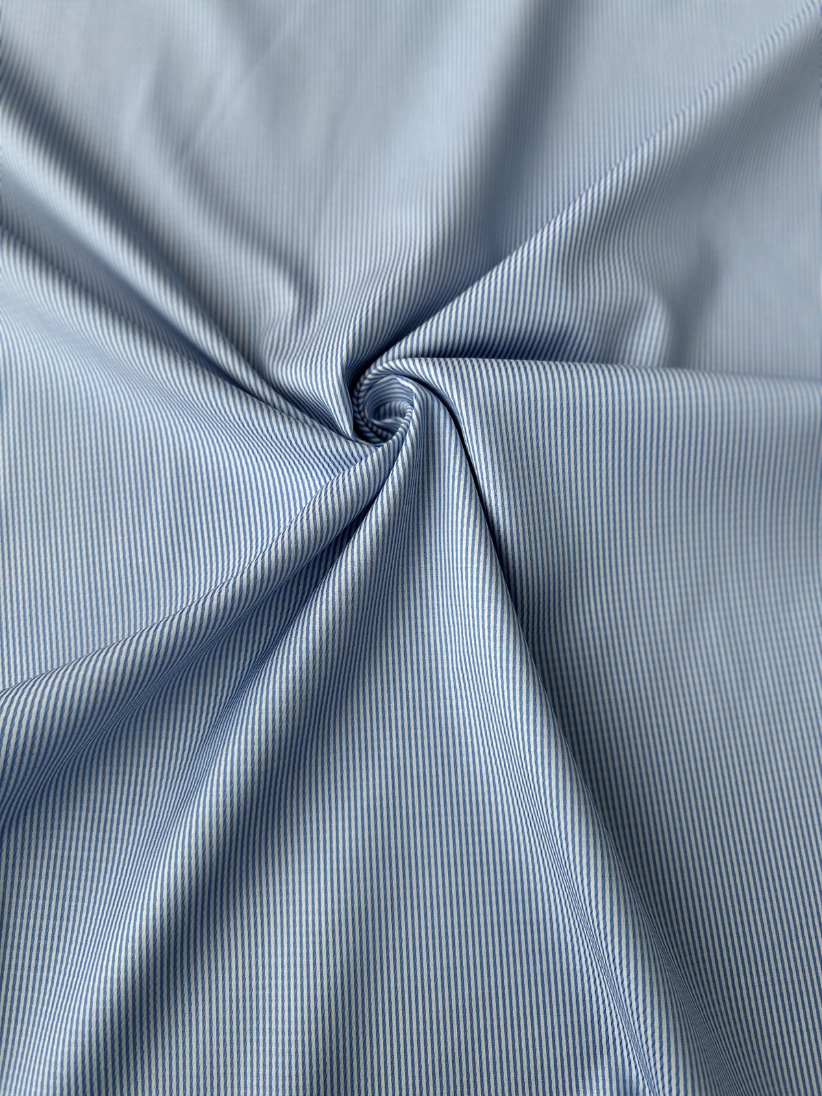 Light blue and white narrow striped fabric draped in a spiral pattern to show texture and drape.