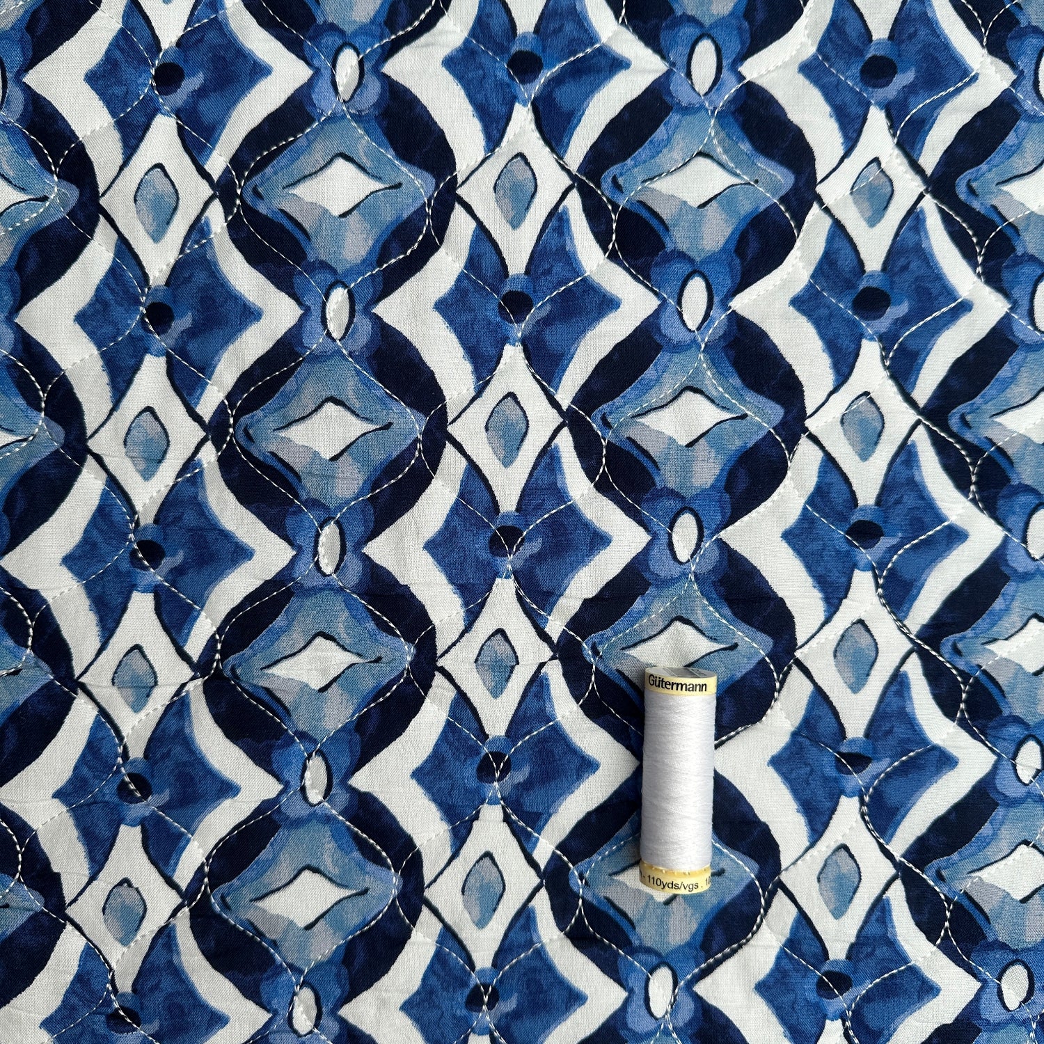 Reel of thread for scale on quilted blue diamond viscose fabric