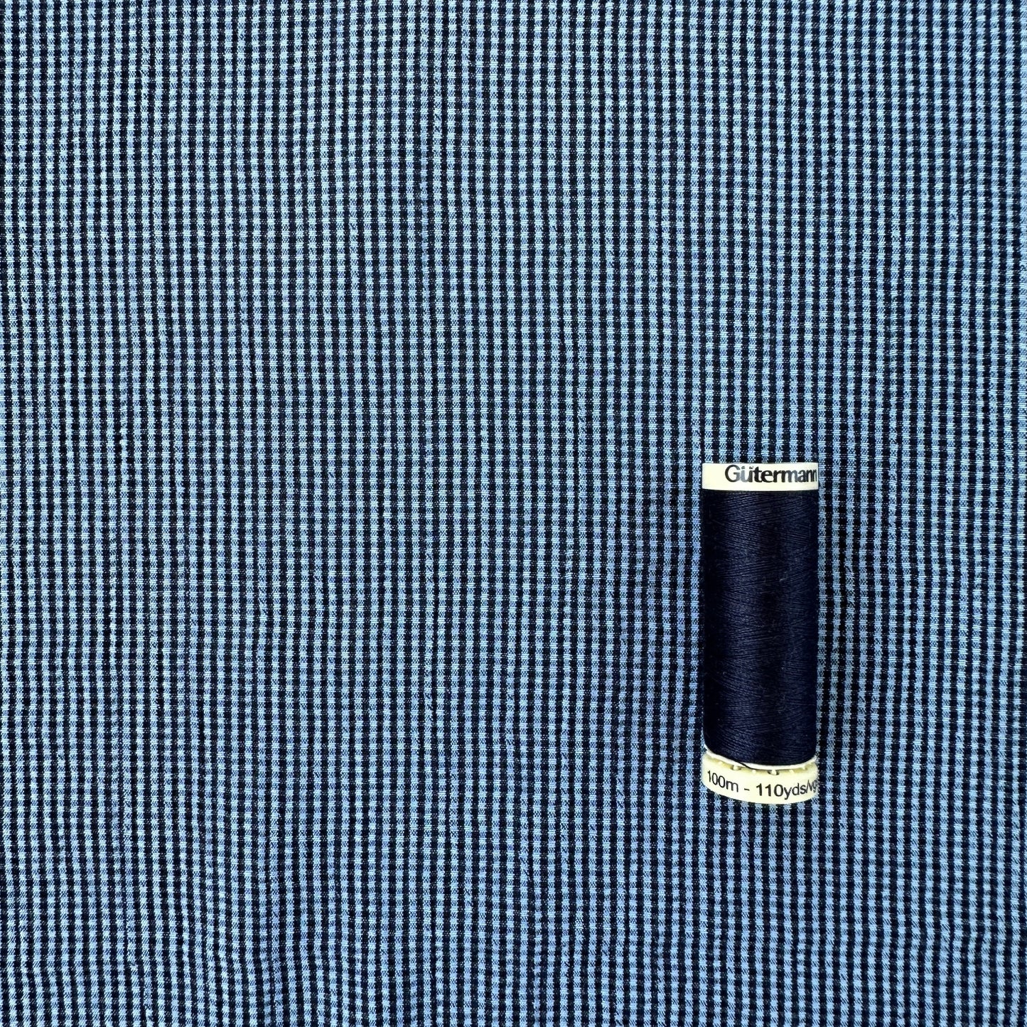 Reel of thread to show scale of blue and navy gingham textured viscose blend fabric