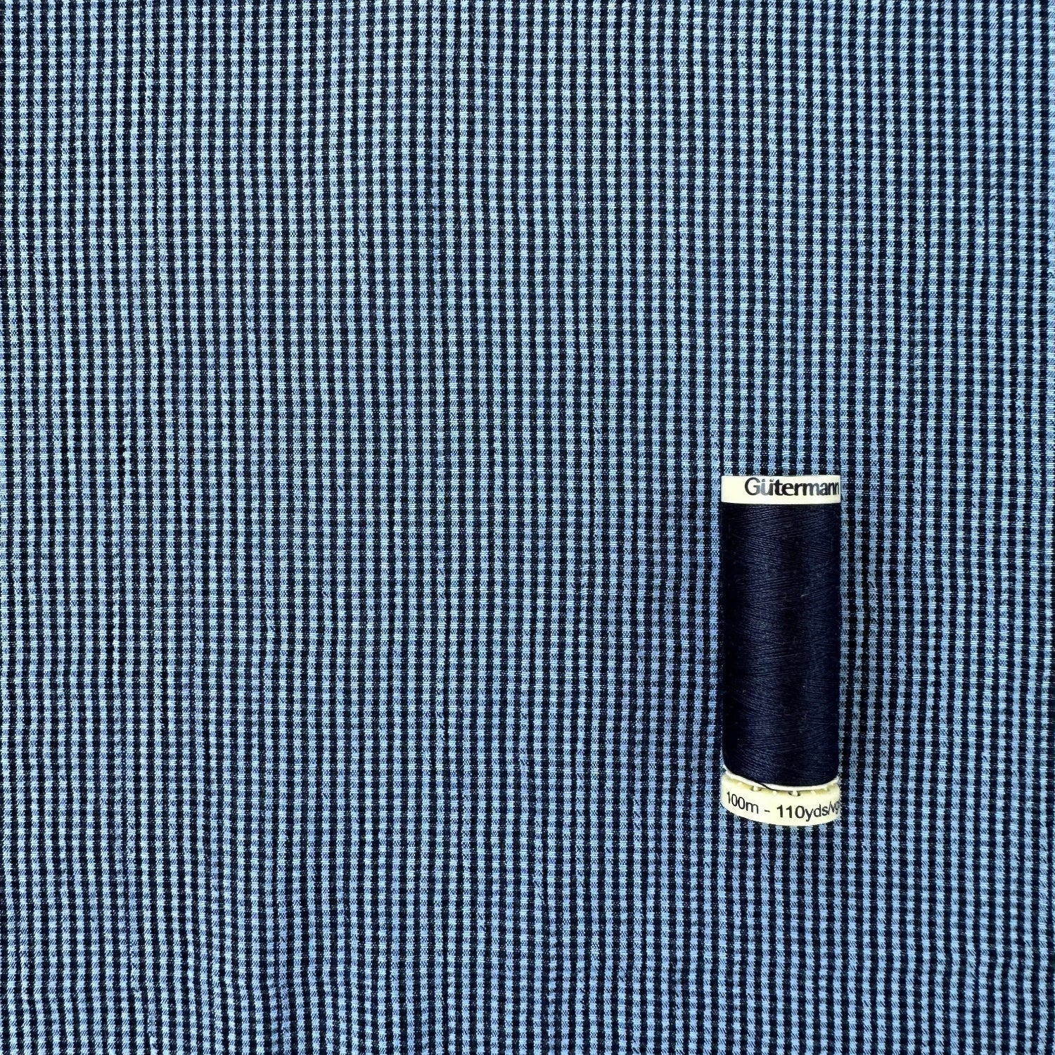 Reel of thread to show scale of blue and navy gingham textured viscose blend fabric