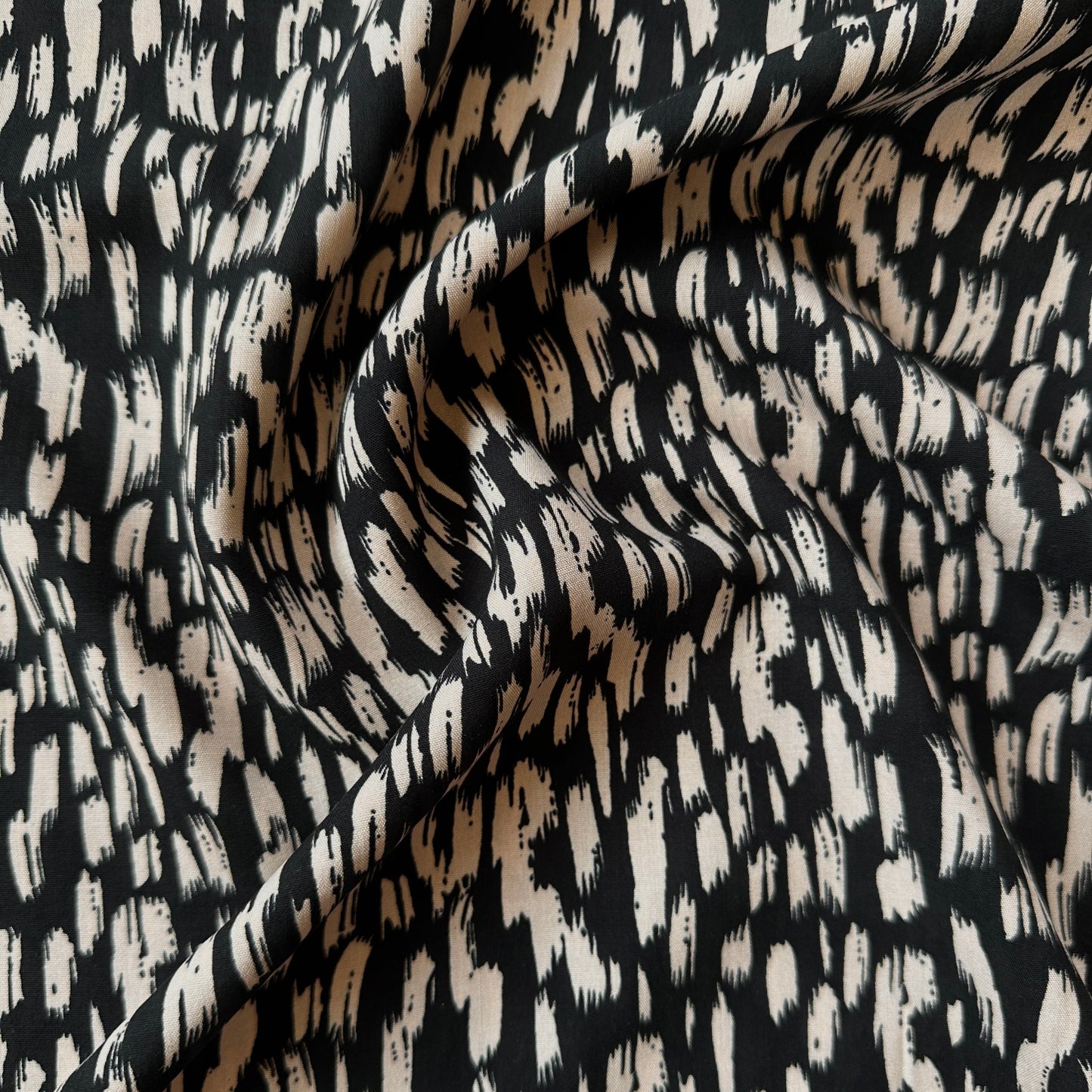 Black and beige abstract patterned fabric with a textured, brushstroke-like design, shown with soft folds.
