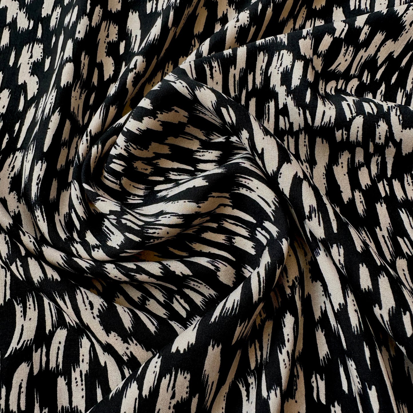 Black and beige abstract patterned fabric with a flowing, draped texture.