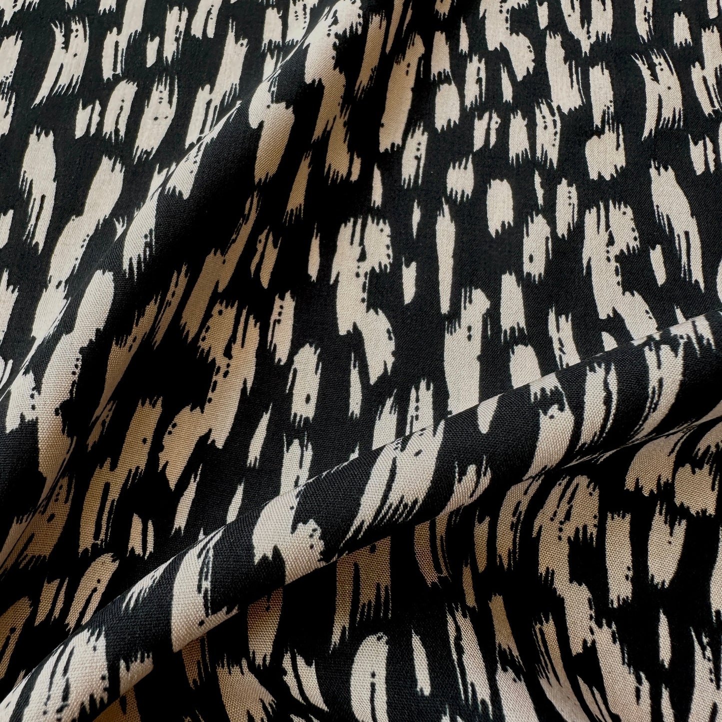 A close-up of draped fabric with an abstract black and beige brushstroke pattern.