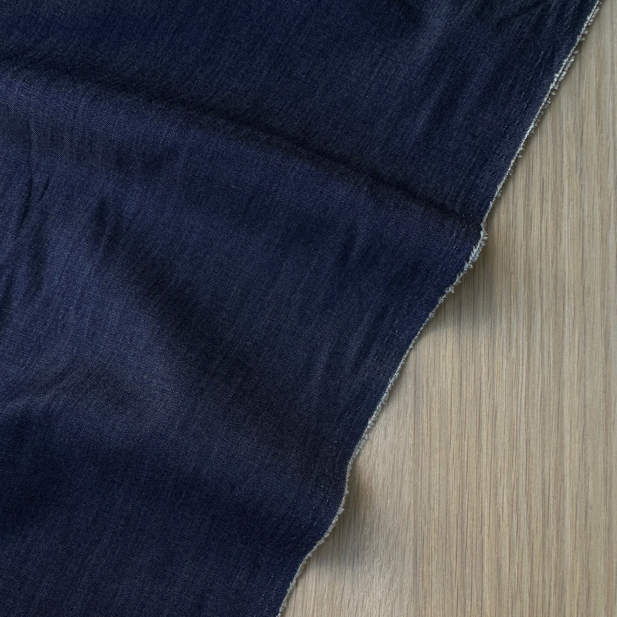 A close-up of dark navy blue denim fabric draped over a light wood surface,