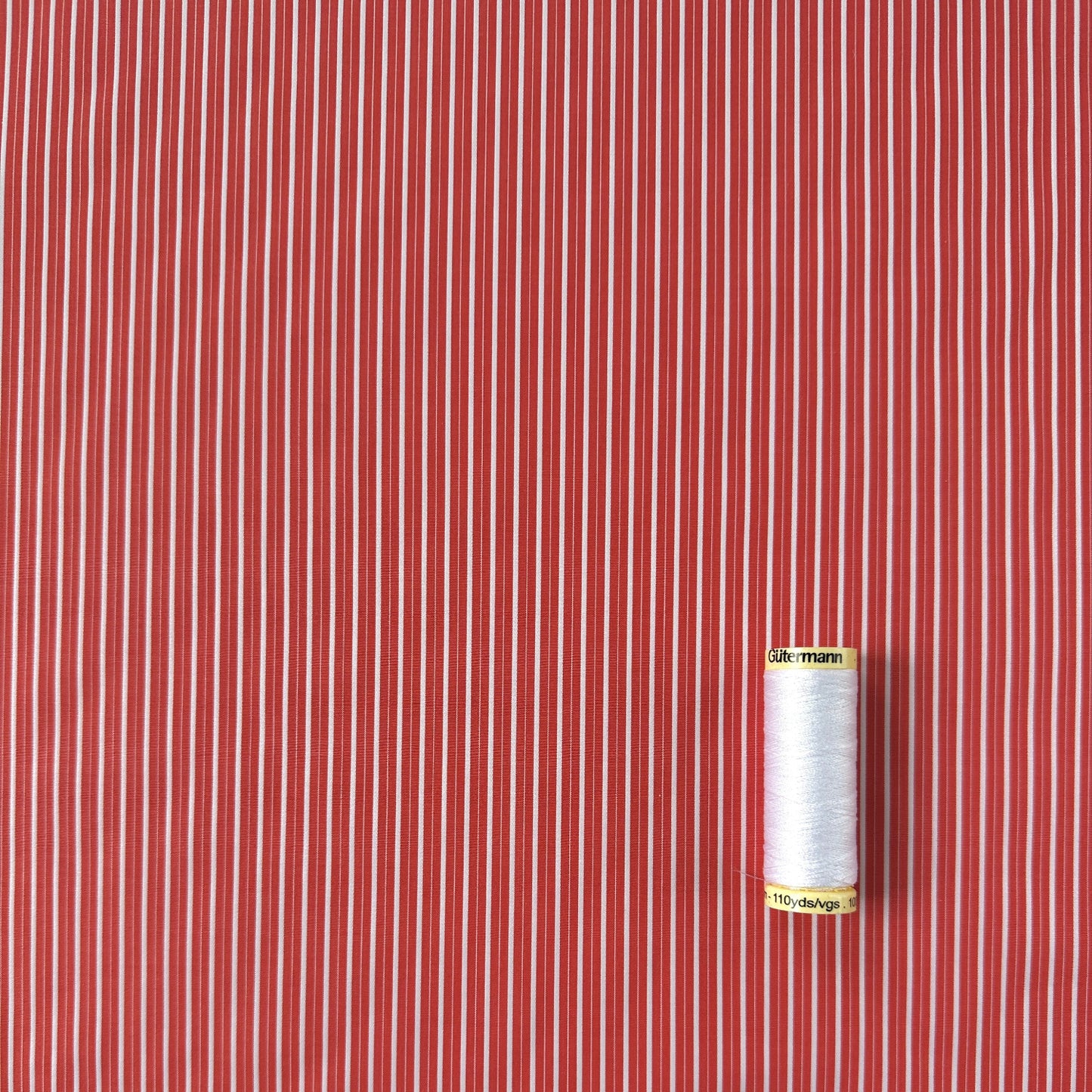 Coral and white striped fabric with a spool of white thread for scale