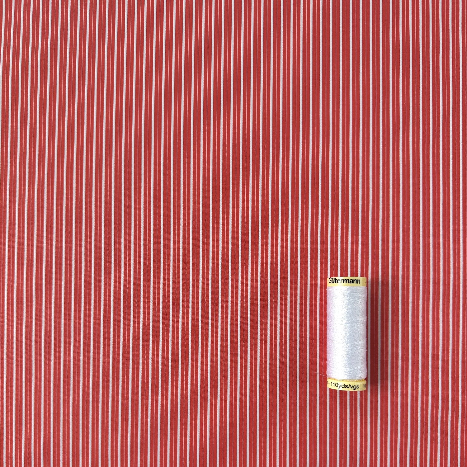 Coral and white striped fabric with a spool of white thread for scale