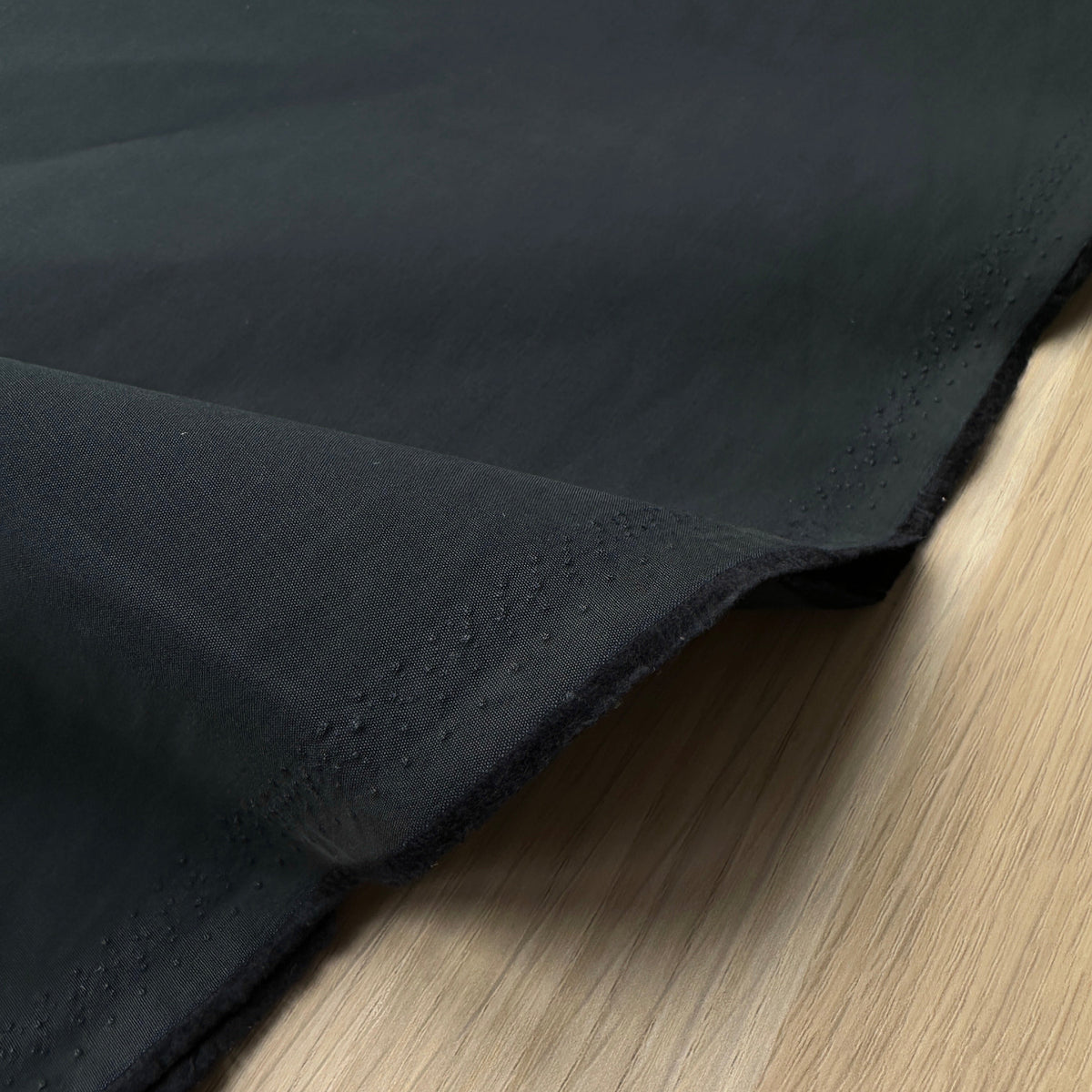 A close-up of a dark navy fabric material on a wooden table