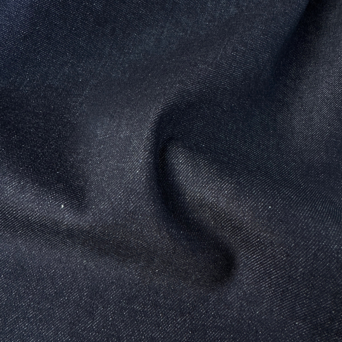 A close-up of dark navy blue denim fabric with a fine twill texture, showing soft folds and shadows.