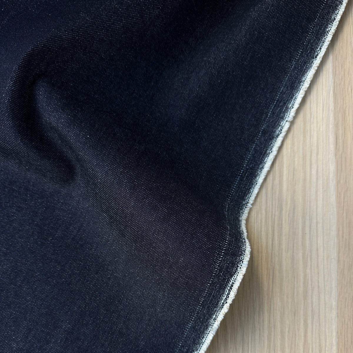 A close-up of a dark indigo denim fabric, showing the texture and selvedge edge