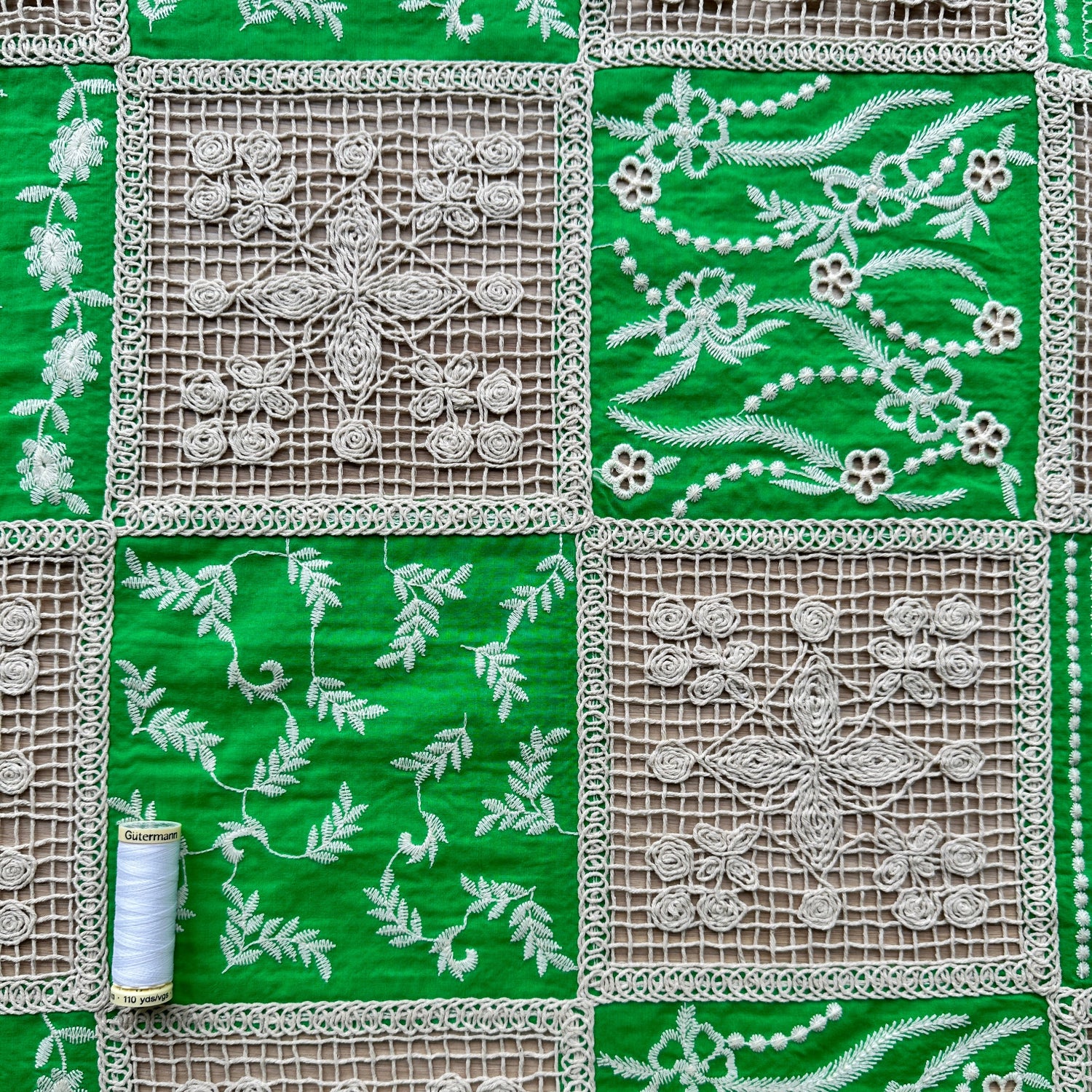 Green and beige fabric with floral lace patterns with a reel of thread for scale