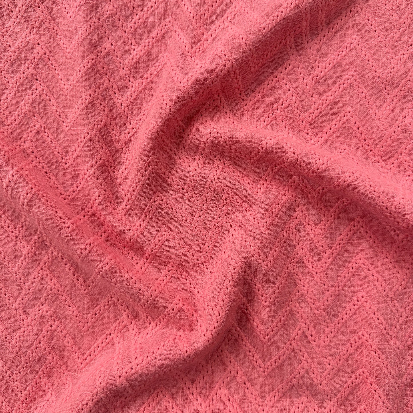 A close-up of textured pink fabric with a repeating chevron or zigzag woven pattern and soft folds.