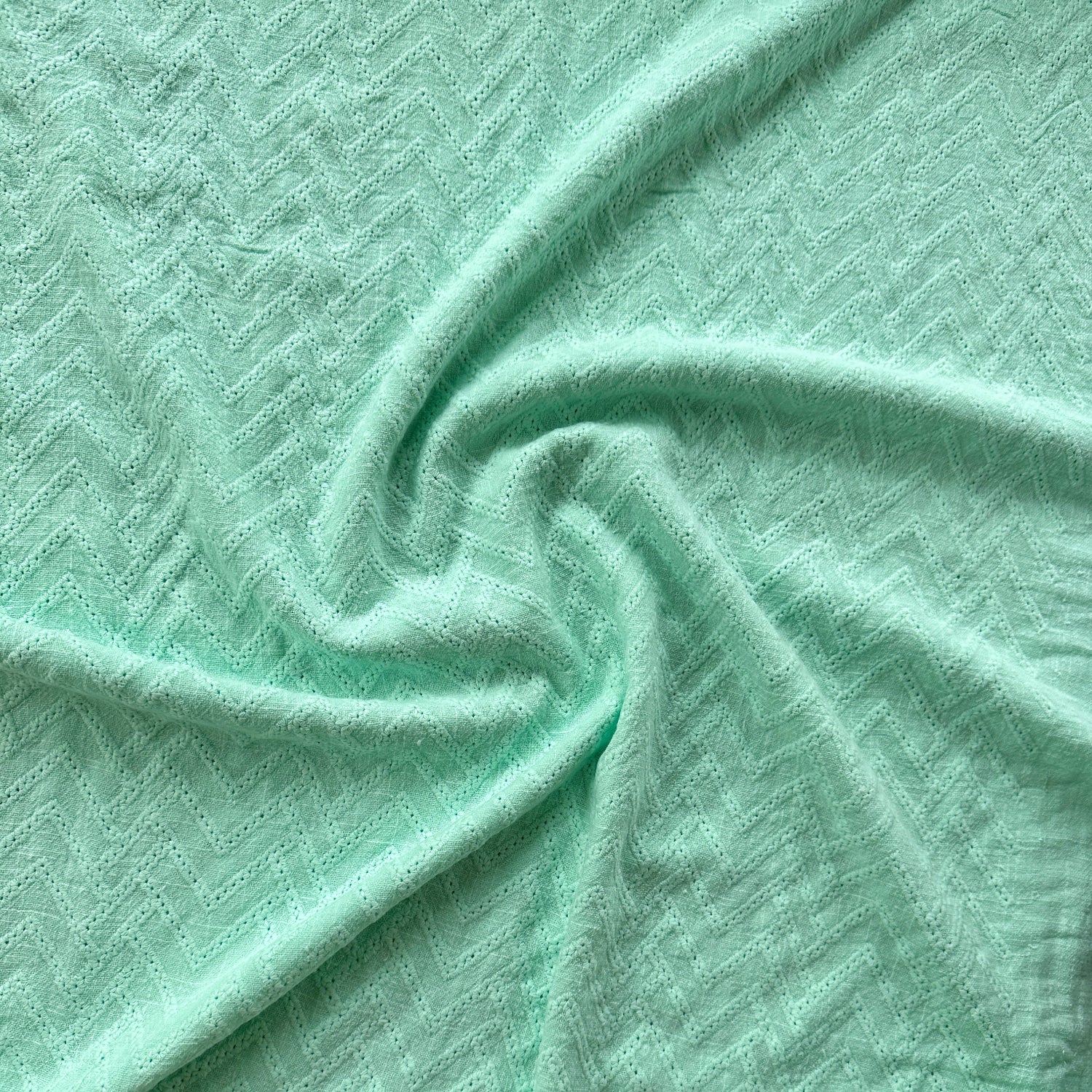 A close-up of mint green textured fabric with a subtle woven pattern, draped in soft folds