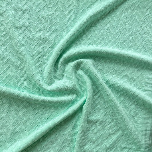 A close-up of mint green textured fabric with a subtle woven pattern, draped in soft folds
