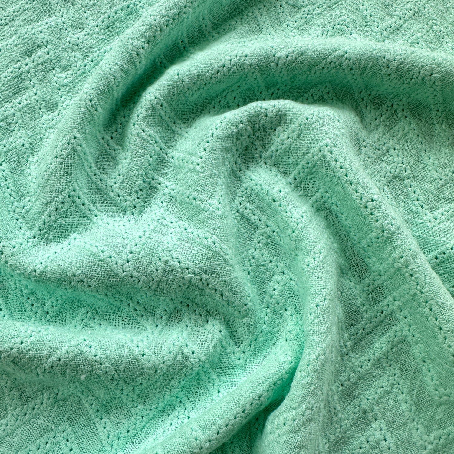 A close-up of mint green textured fabric with zigzags embroidered across it