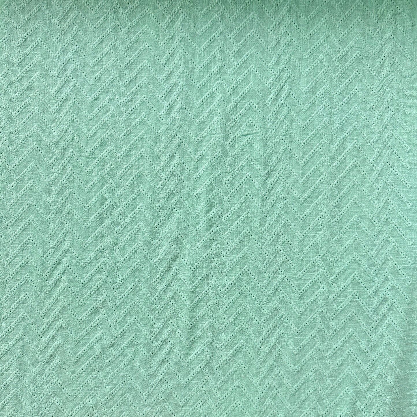 A close-up of a mint green textured cotton fabric with a subtle herringbone pattern