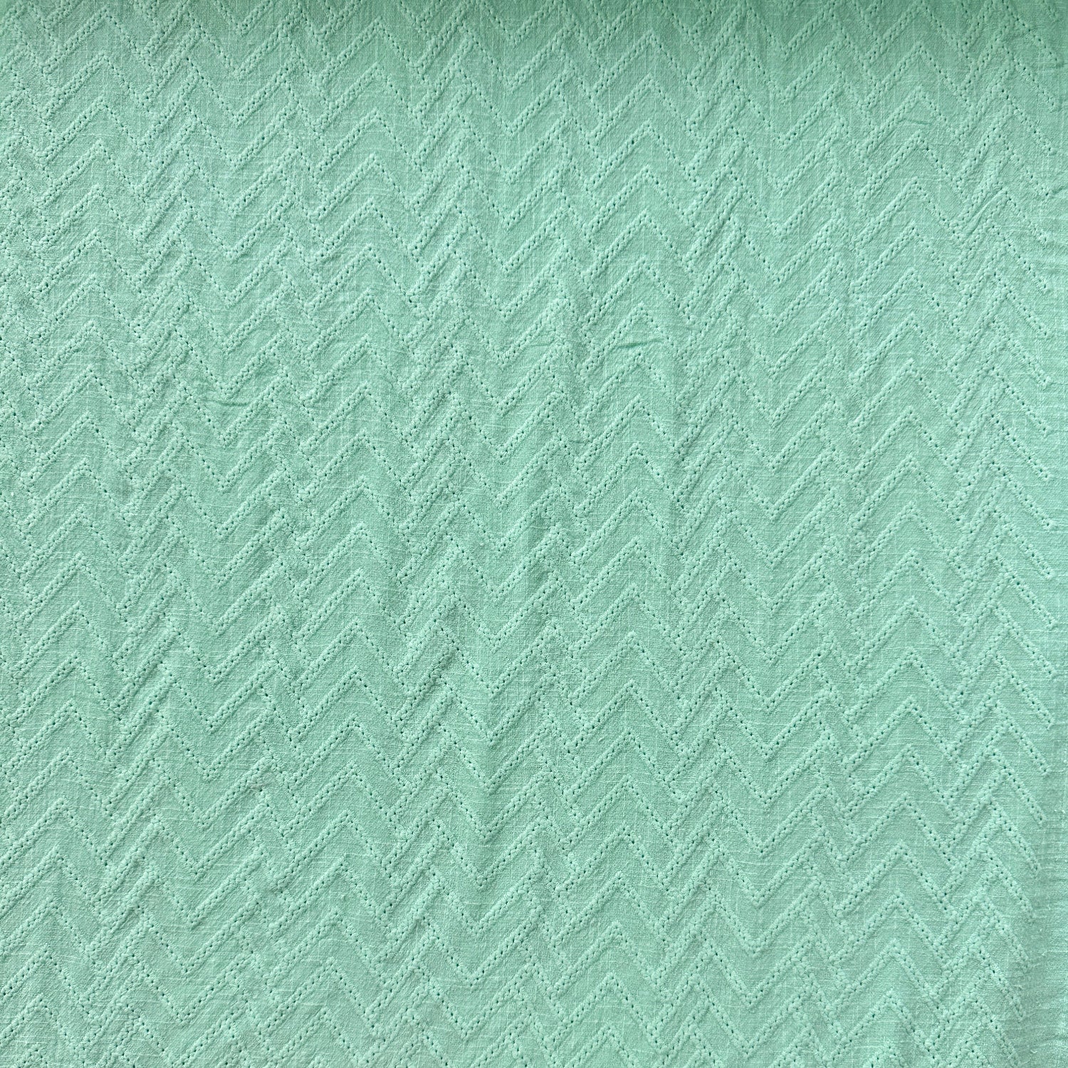 A close-up of a mint green textured cotton fabric with a subtle herringbone pattern