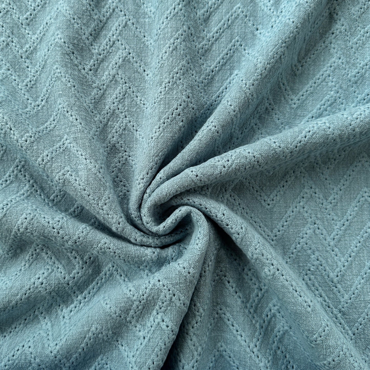 A close-up of a blue textured fabric with embroidered zigzags across it
