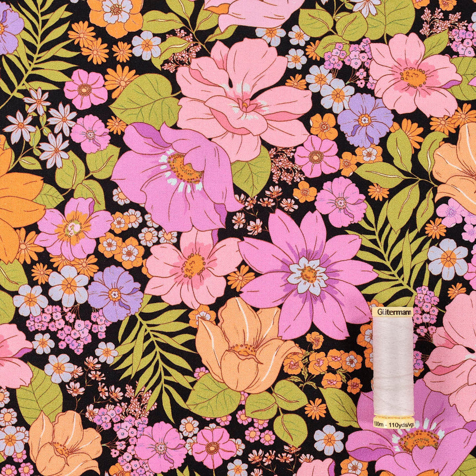 Pink and orange flowers across a black background with reel of thread for scale