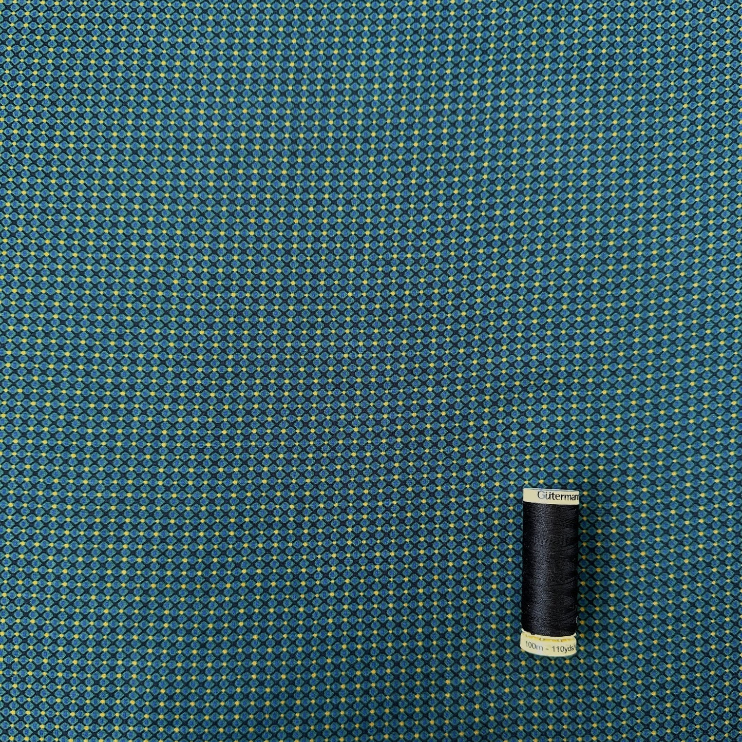 Reel of gutermann thread showing scale of diamond pattern on dressmaking fabric