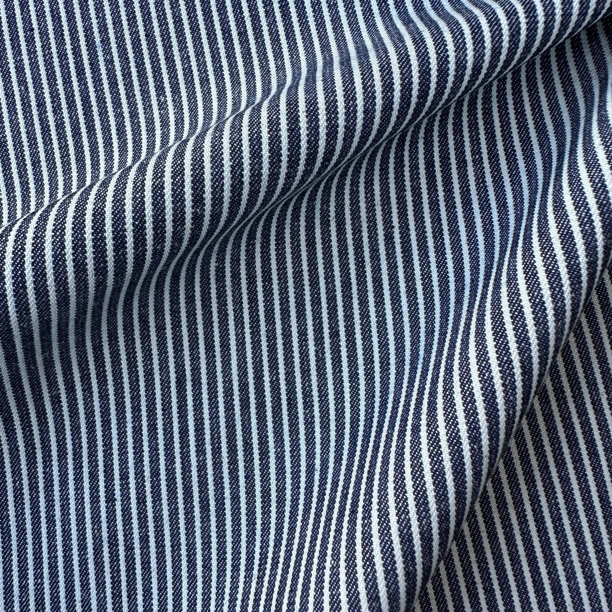 A close-up of a woven denim fabric with a vertical stripe pattern in navy blue and off-white, showing soft folds and texture.