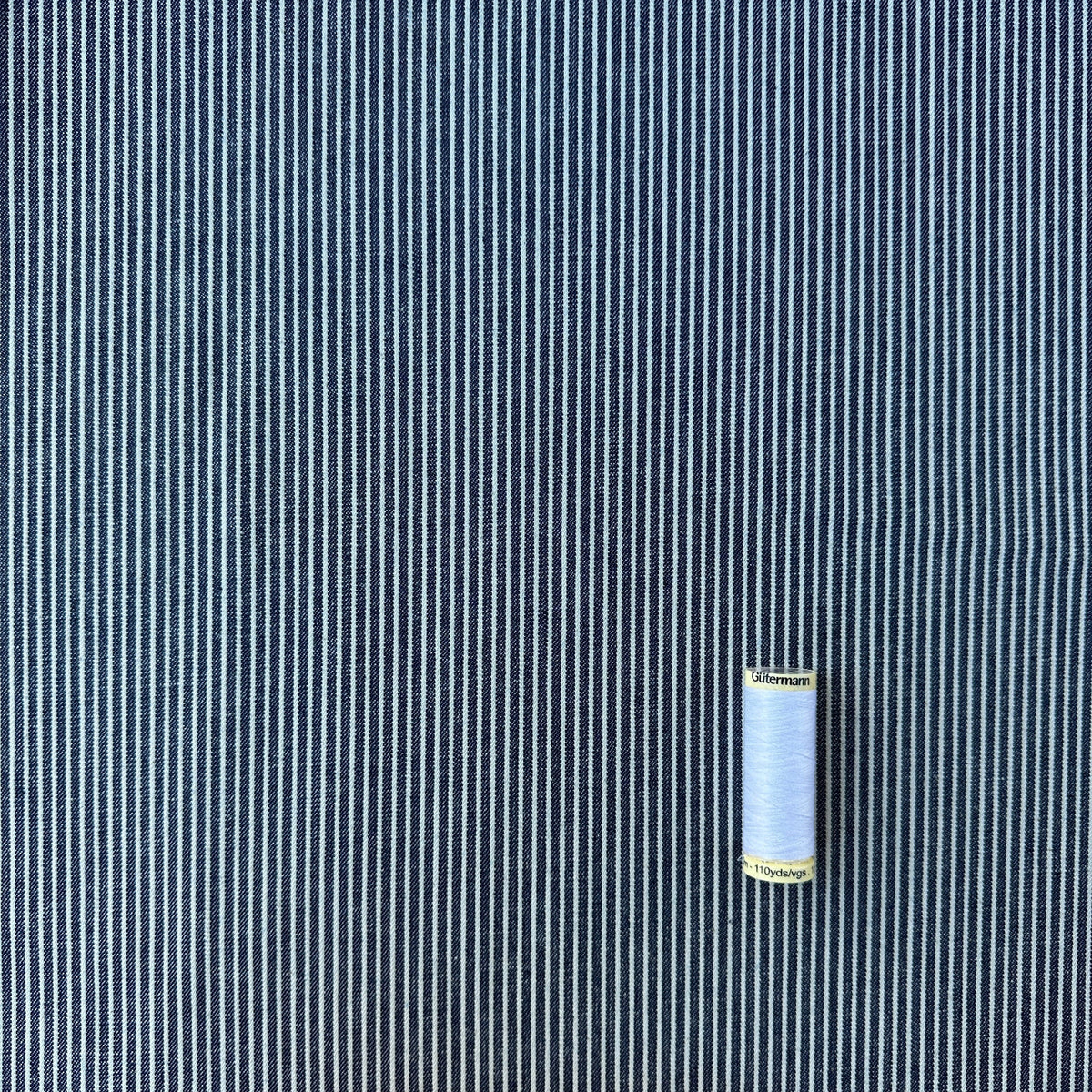 Navy blue and white vertically striped denim fabric with a spool of white thread for scale