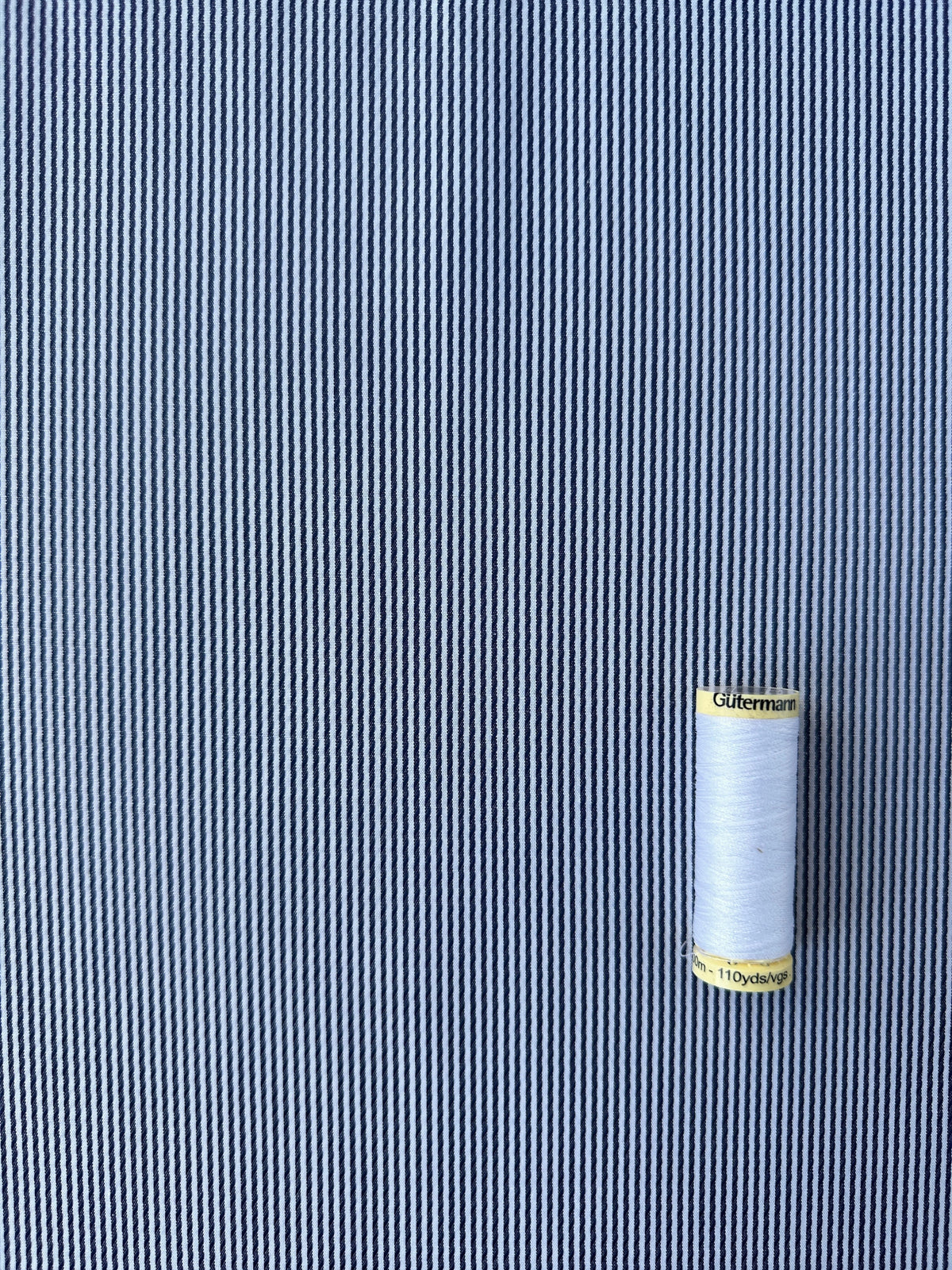 A spool of white thread placed on a navy and white striped fabric background.