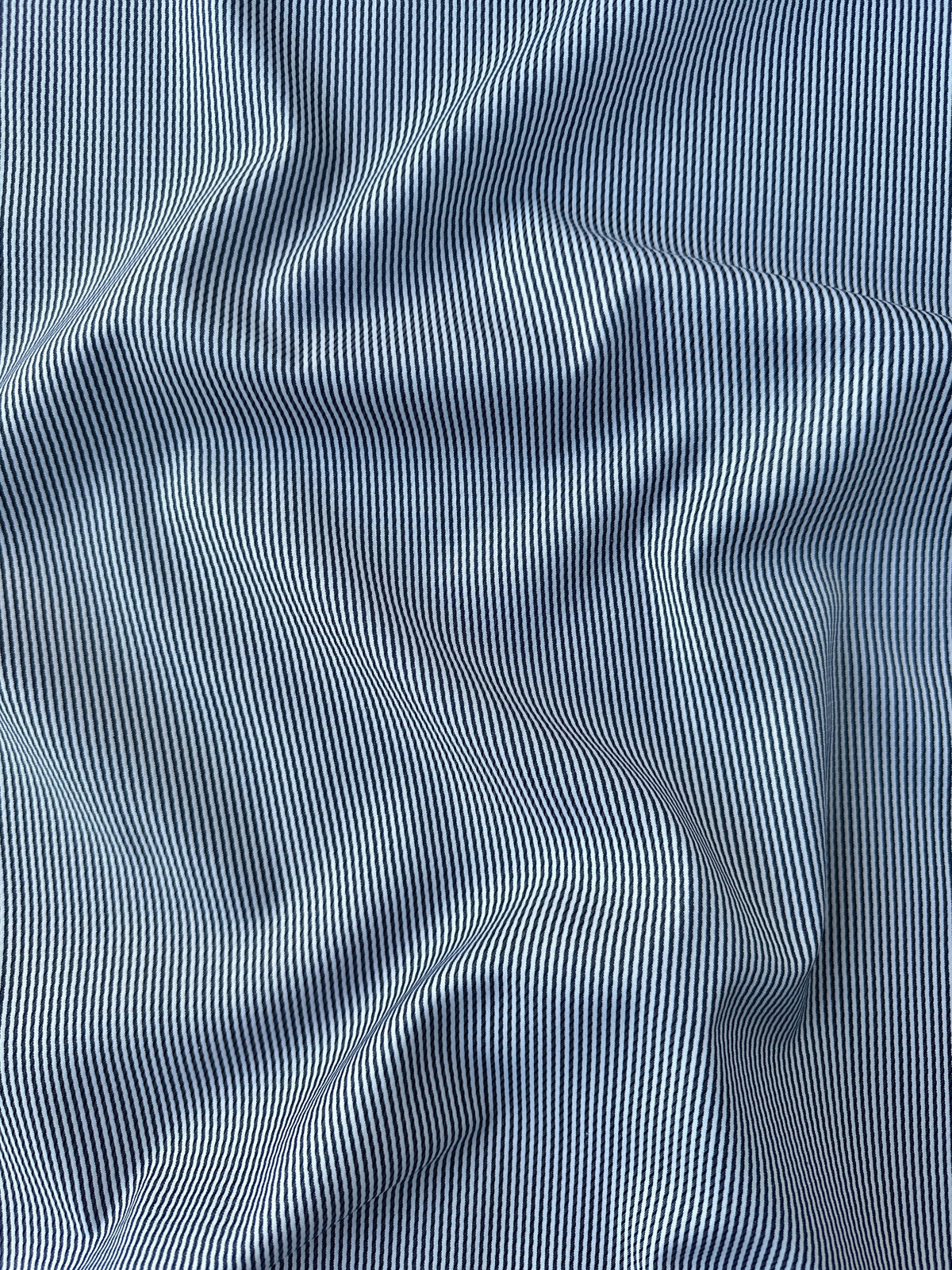 A close-up of draped blue and white striped fabric, showing the fine vertical stripe pattern and soft folds.