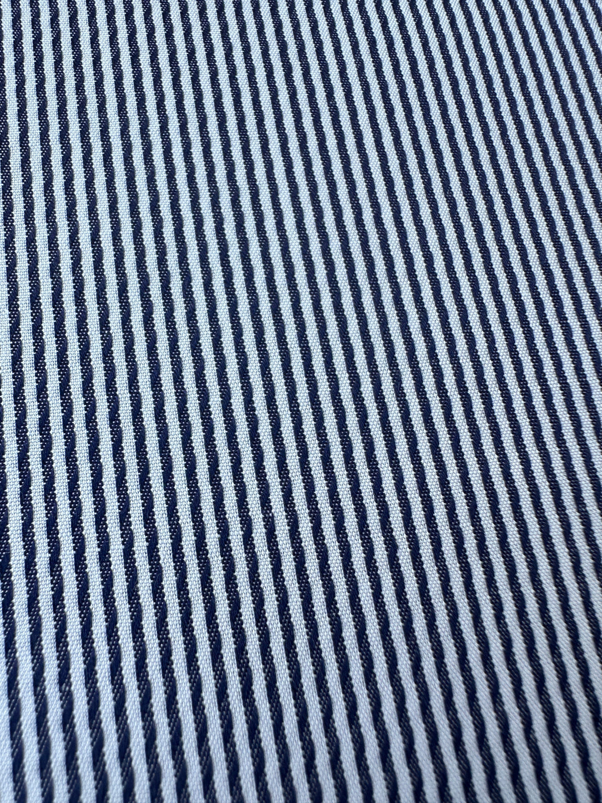 A close-up of a woven fabric with narrow vertical navy blue and white stripes.