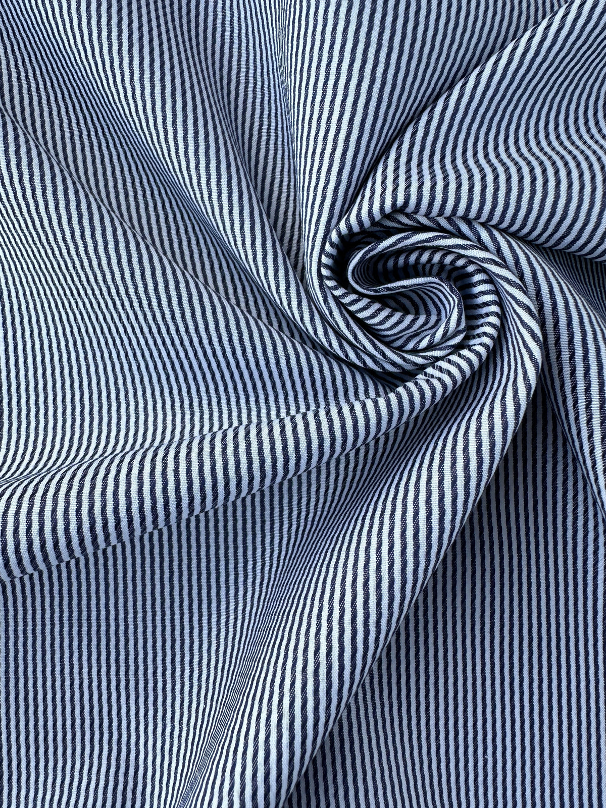 A close-up of striped fabric arranged in a spiral, showing narrow vertical stripes in dark blue and white.