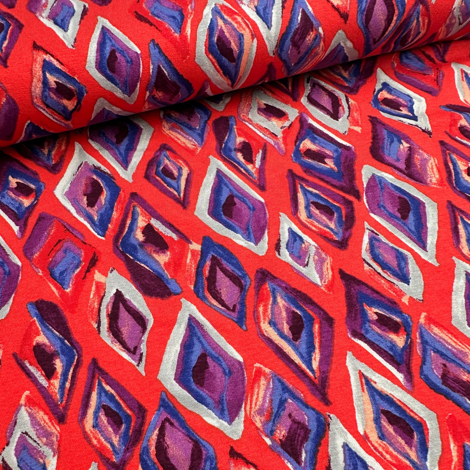 Fabric with a geometric pattern of red, purple, and grey diamonds.