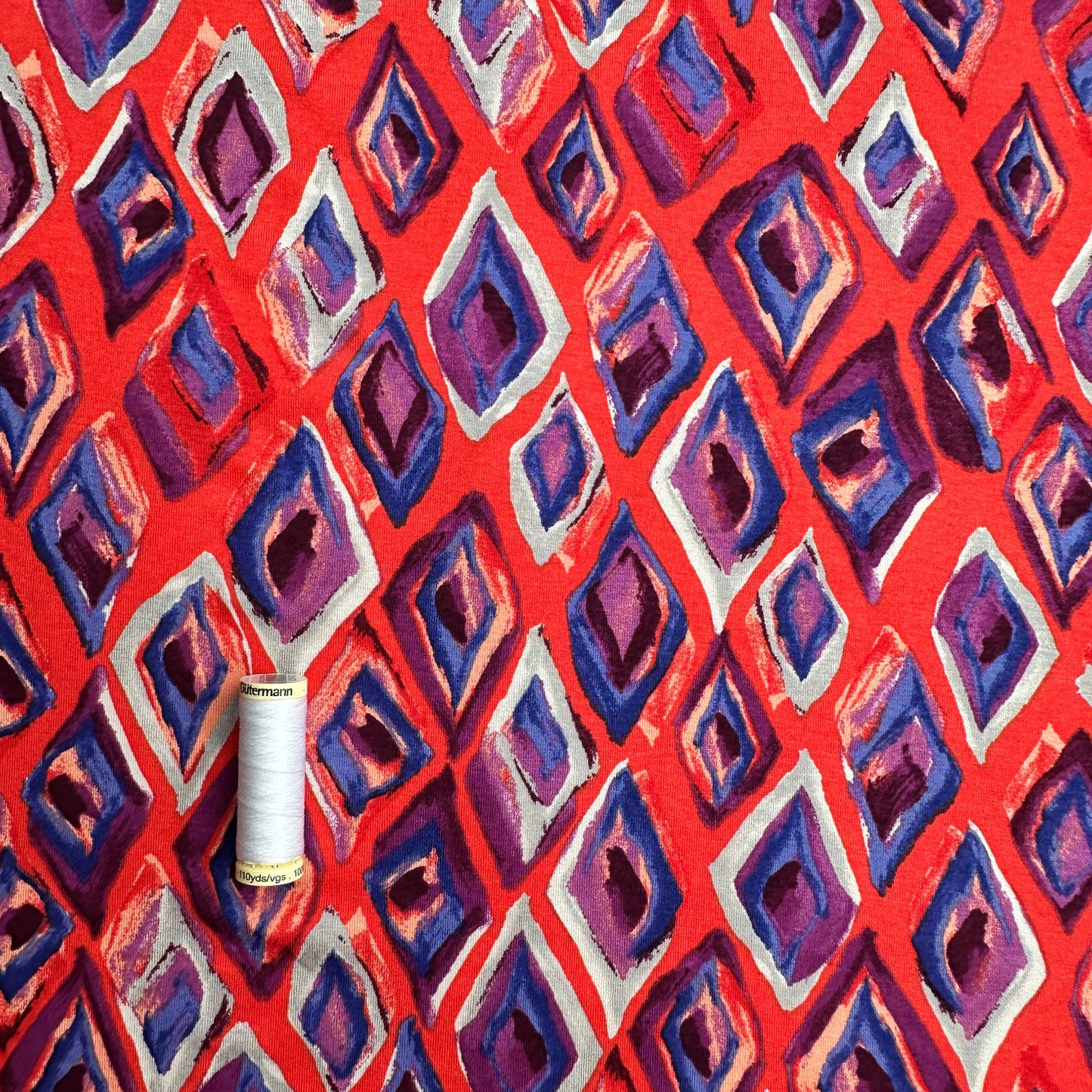 Thread spool on a red, grey, purple and  blue geometric patterned background