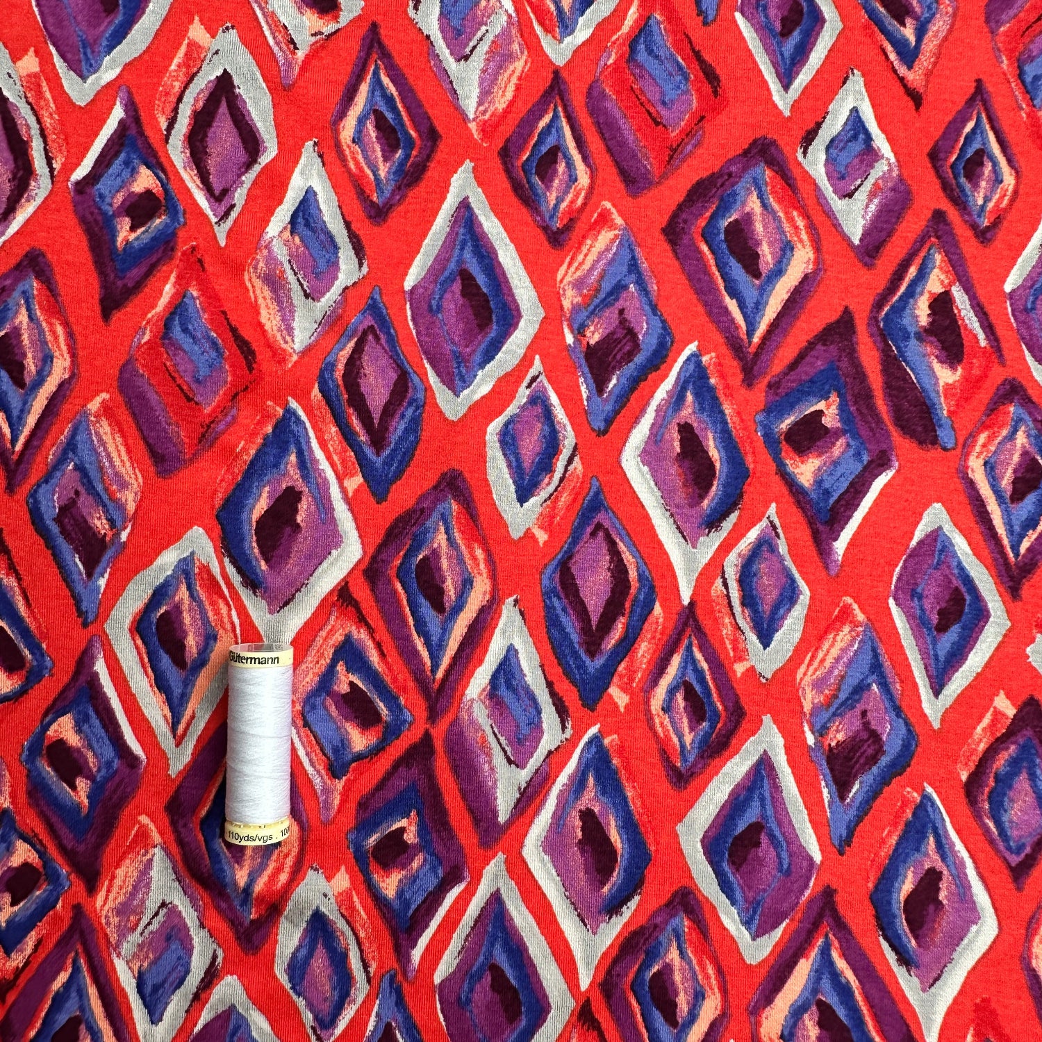 Thread spool on a red, grey, purple and  blue geometric patterned background