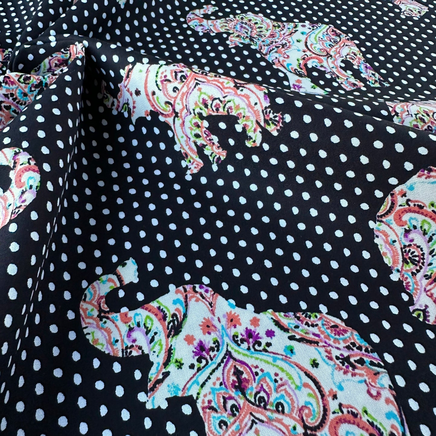 Fabric with polka dots and colourful paisley elephants on a black background